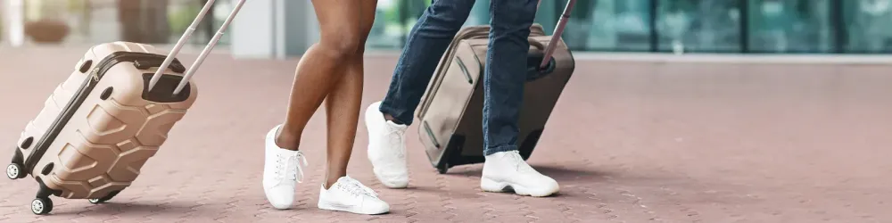A couple walks through an airport terminal, each pulling a suitcase behind them.